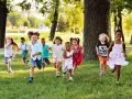 Des enfants joyeux courent dans l'herbe, profitant d'une journée ensoleillée dans une colonie de vacances 3-6 ans.