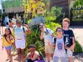 Des enfants joyeux font des signes de paix devant une attraction, un avis "supernova juniors" est visible.