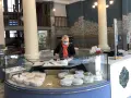 Une fromagère masquée prépare des fromages dans une vitrine réfrigérée.