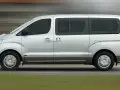 Un mini bus argenté roule sur une route. Ce véhicule spacieux est idéal pour les familles ou les groupes, et peut être conduit avec un permis B.