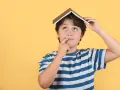 Un enfant de 5 ans, avec un livre sur la tête, réfléchit. Il est en colonie de vacances.