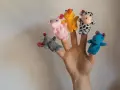 Main d'une personne avec cinq marionnettes à doigts en feutrine : souris grise, lapin rose, canard jaune, vache noire et blanche, hippocampe bleu.