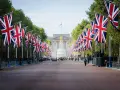 Allée bordée de drapeaux britanniques menant à un palais, avec des arbres et des gardes.