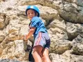 Enfant souriant escaladant un rocher avec un casque bleu.