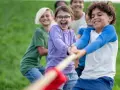 Des enfants joyeux jouent à la corde dans un champ d'herbe verte.