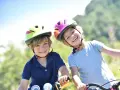 Deux enfants souriants, casques de vélo colorés, profitent de leurs vacances scolaires en Savoie.