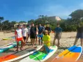 Un groupe d'adolescents et un moniteur sur une plage avec des planches de paddle.