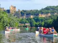 Des gens en canoë sur une rivière, avec un château en arrière-plan.