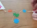 Fabrication d'un cerf-volant étoile : fils, formes colorées (étoiles, ovales, octogone) et mains.
