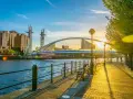 Promenade ensoleillée au bord de l'eau, avec un pont moderne et des bâtiments reflétant le soleil. Idéal pour visiter Manchester ou Liverpool.