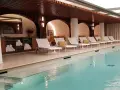 Piscine intérieure avec chaises longues blanches, coussins jaunes et étagères de serviettes.