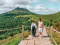 Couple marchant sur un chemin en bois avec un volcan en arrière-plan en Auvergne.