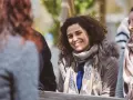 Une femme souriante aux cheveux bouclés porte une écharpe et une veste à capuche en fourrure.