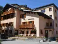 Bâtiment de style alpin avec balcons en bois et volets marrons, fleuri. Une enseigne "La Joie de Vivre" suggère une ambiance de colonie en Haute-Savoie.