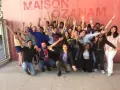 Un groupe de jeunes gens, dont un prêtre, pose joyeusement devant un mur rose avec le texte "MAISON OZANAM".
