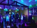 Scène de concert animée avec des lumières colorées. Un groupe joue, avec des chanteurs, un trompettiste et un claviériste. Le public, dont des enfants, filme le spectacle. Ces vacances musicales sans frontières sont une fête pour les sens.
