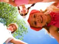 Trois enfants souriants, vus d'en bas, profitent d'une journée ensoleillée lors d'un camp sportif.