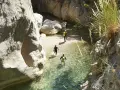 Trois personnes en combinaison font du canyoning dans une rivière aux eaux claires, entourées de falaises rocheuses.