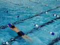 Un nageur utilise une planche bleue dans une piscine avec des lignes de bouées bleues et blanches.