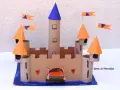 Château fort en carton avec tours, drapeaux orange et bleus, et une herse.