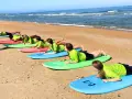 Des adolescents en stage sportif sur la plage, allongés sur des planches de surf, apprenant les bases avant de se jeter à l'eau.