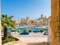 Vue d'un port de plaisance animé à La Valette, Malte, avec des voiliers, des bâtiments historiques et une palme. Parfait pour un séjour à Malte La Valette.
