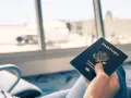 Main tenant une carte d'identité américaine devant une fenêtre d'aéroport avec un avion en arrière-plan.
