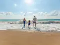Une famille se tient la main sur la plage, profitant des vagues. Ils pensent à devenir famille d'accueil pour les vacances, offrant ces moments de bonheur.