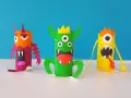 Trois monstres colorés faits à la main, en rouleaux de papier toilette, sur fond bleu.