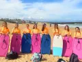 Huit jeunes filles en t-shirts orange, prêtes pour leur colonie à la mer, posent avec leurs bodyboards sur la plage.
