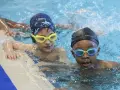 Deux enfants avec des bonnets et lunettes de natation dans une piscine.