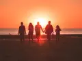 Une famille profite de ses vacances à l'étranger, marchant main dans la main sur une plage au coucher du soleil.