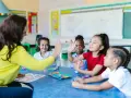 Une enseignante donne une tape dans la main à des enfants autour d'une table dans une salle de classe.