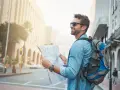 Un homme souriant avec un sac à dos consulte une carte, prêt pour un voyage en immersion dans la ville.