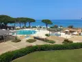 Piscine et transats dans un complexe hôtelier en bord de mer, sous un ciel bleu.