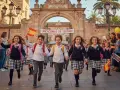 Des écoliers joyeux courent sous des confettis devant une arche ornée d'une banderole "¡VACACIONES DE SERANO!".