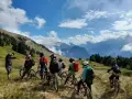 Groupe d'ados en colonie VTT descente, prêts à dévaler les pentes montagneuses sous un ciel bleu éclatant.