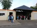 Des enfants font la queue devant un bâtiment scolaire, certains avec des sacs à dos.