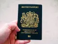 Main d'une personne tenant un passeport britannique bleu foncé avec le blason royal doré.