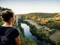 Une femme admire un paysage de carte postale lors de son voyage découverte en France. La rivière serpente à travers des collines verdoyantes et des villages pittoresques.