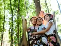 Quatre enfants souriants portant des casques de sécurité dans un parc d'aventure.