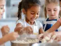 Des enfants joyeux préparent une recette dans des tabliers, les mains couvertes de farine.