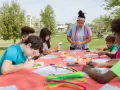 Des enfants créent des œuvres d'art en plein air autour d'une table recouverte d'une nappe orange.