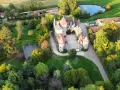 Vue aérienne d'un château entouré d'arbres, avec un étang et un terrain de sport.
