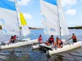 Des jeunes profitent d'une colonie de vacances voile, naviguant sur des catamarans par une journée ensoleillée.