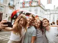 Quatre jeunes souriants prennent un selfie à Londres, avec un bus rouge et des drapeaux britanniques en arrière-plan.