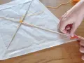 Mains fabriquant un cerf-volant en papier blanc avec des bâtons de bois et de la ficelle.