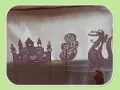 Théâtre d'ombres : château, arbre et dragon en papier, manipulés par une main.