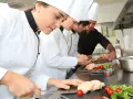 Des chefs apprennent la réglementation atelier cuisine en préparant des mets. Ils coupent du foie gras, des tomates cerises et de la salade.