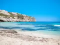Plage de Majorque avec eaux turquoises, falaises et bâtiments blancs à flanc de colline.